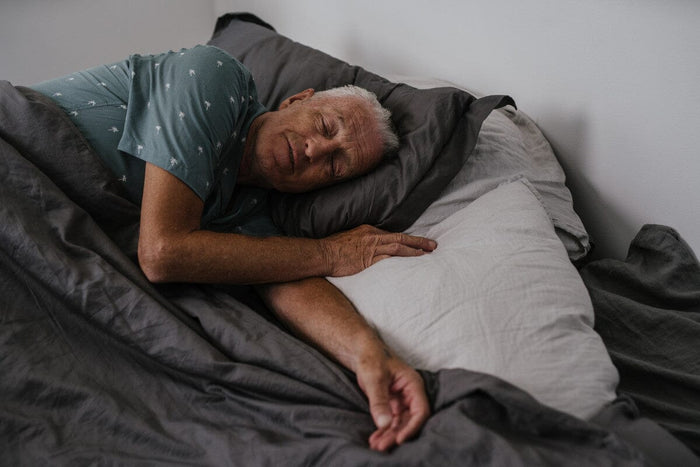 senior man sleeping peacefully under a gray comforter.
