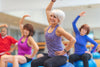 several older folk sitting on exercise balls in a workout class, stretching their arms and backs.