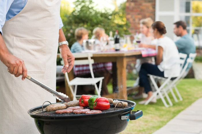 close-up of a senior cooking veggies, turkey patties, and sweet potatoes on a grill.