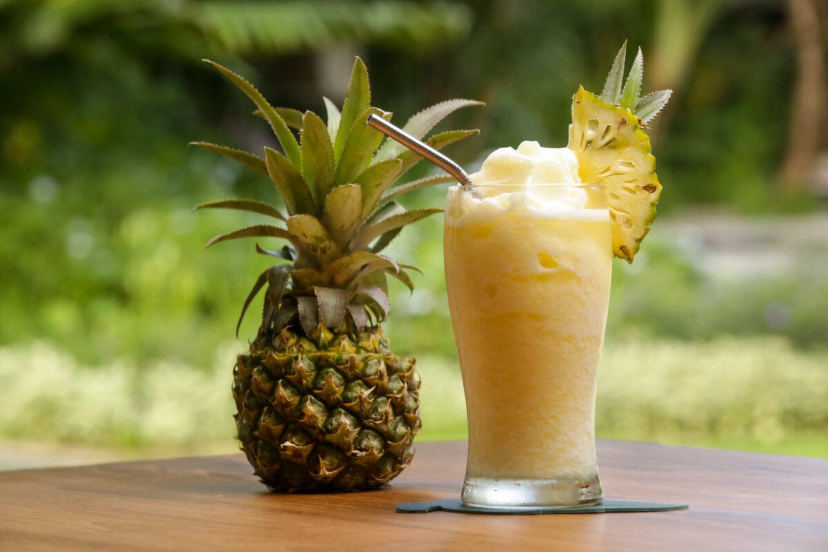 a pineapple and a pineapple smoothie sitting next to each other on a wooden table outside.