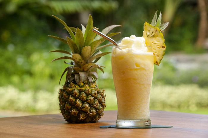 a pineapple and a pineapple smoothie sitting next to each other on a wooden table outside.