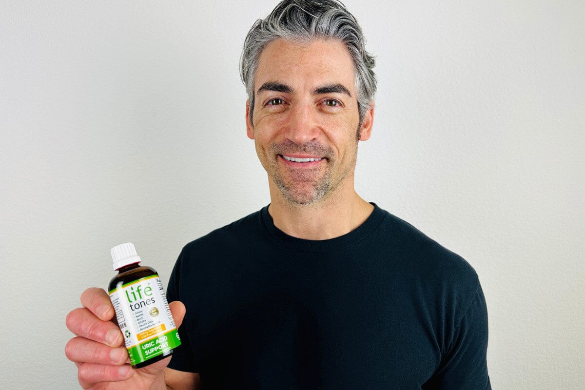 man smiling and holding up a bottle of Lifetones Uric Acid Support Tincture.