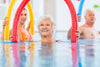 senior woman exercising in the pool with a red pool noodle.