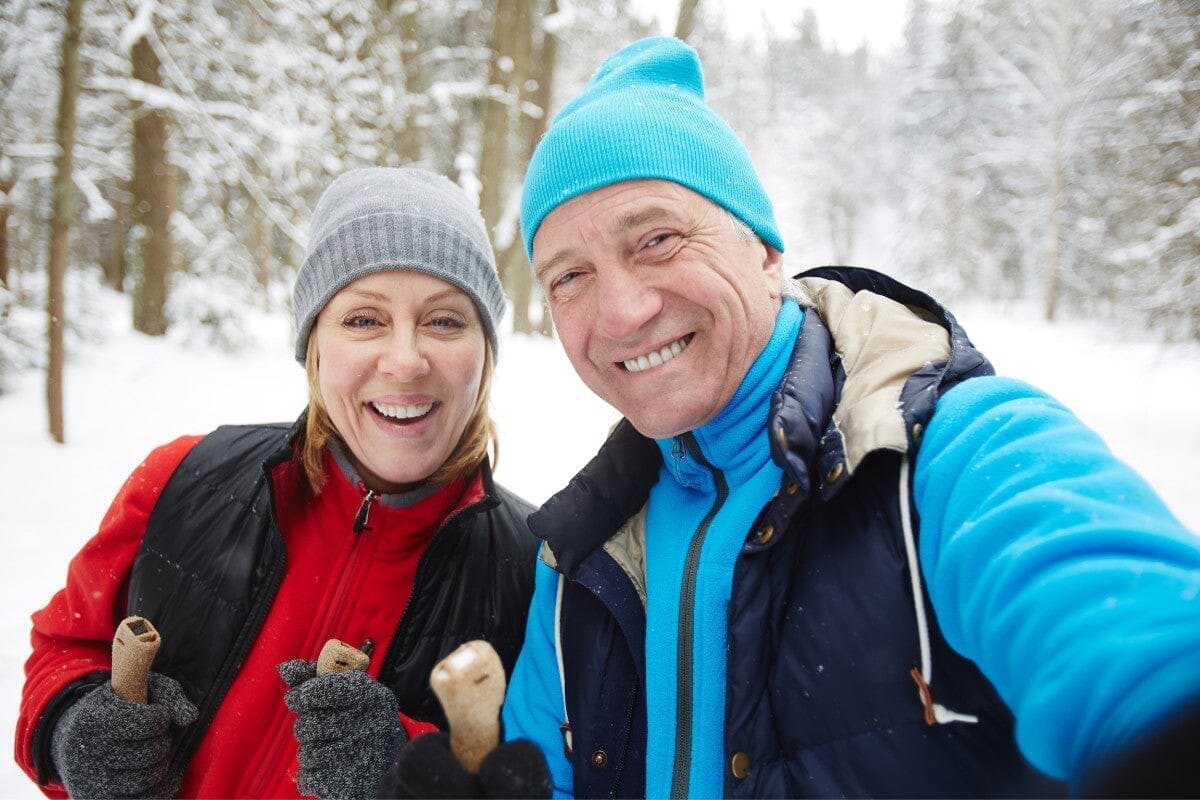 senior couple smiling for a picture while outside in the snow hiking.