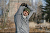 senior man dressed in a gray sweater and green beanie, stretching outside in the cold weather.