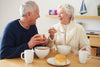 senior couple laughing and smiling as they have some soup and bread for lunch.