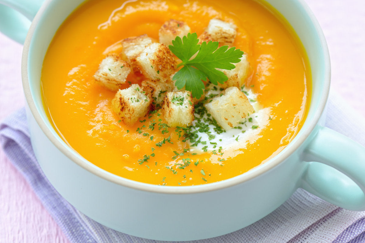white mug full of pumpkin soup with croutons on top